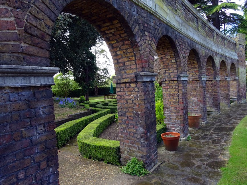 A historic castle with ornate architectural details and multiple turrets, surrounded by meticulously maintained formal gardens featuring neatly trimmed hedges, geometric flower beds, and lush green la